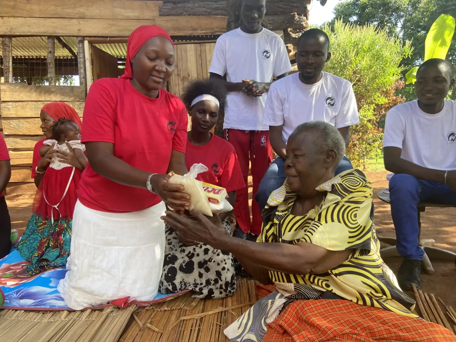 Volunteers giving supplies to an elderly woman seated on a mat
